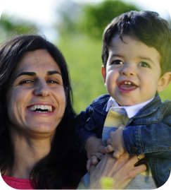 mother holding a child with achondroplasia, both smiling outdoors