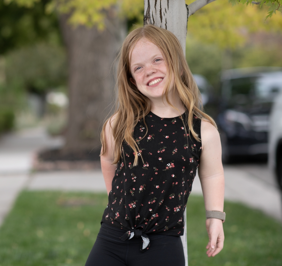 a smiling young girl from the achondroplasia community, standing outdoors, embodying confidence and joy