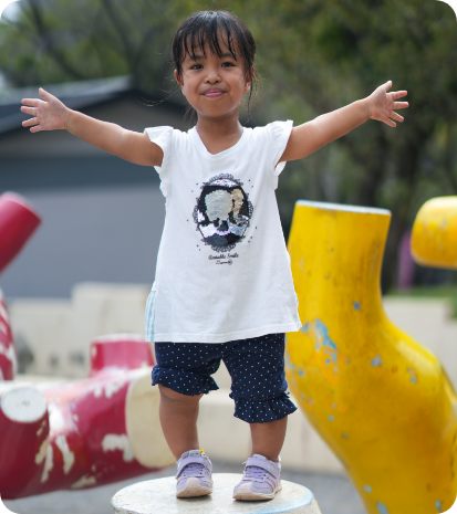 child with achondroplasia posing with arms outstretched on a playground