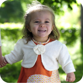 young girl with achondroplasia standing in a park, smiling happily