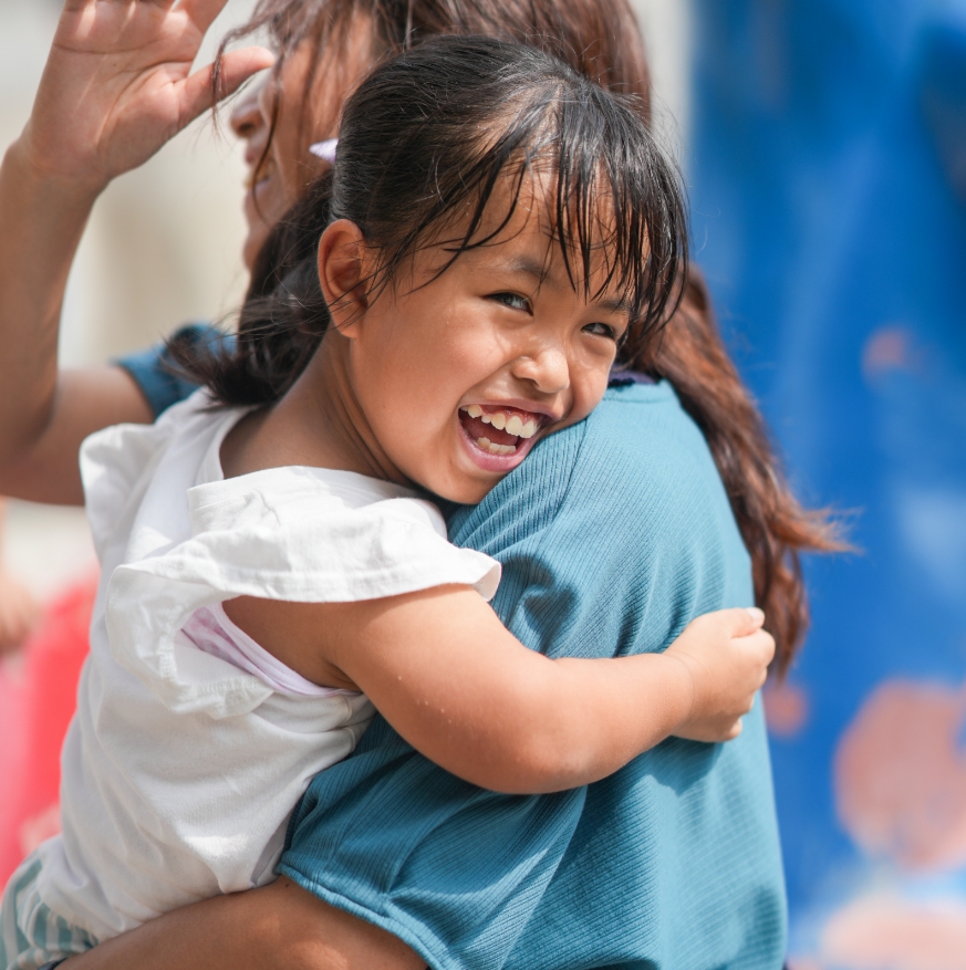 child with achondroplasia smiling while being carried outdoors